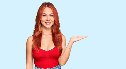 Young redhead woman wearing casual clothes smiling cheerful presenting and pointing with palm of hand looking at the camera.