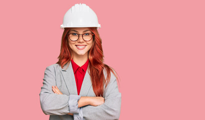 Young redhead woman wearing architect hardhat happy face smiling with crossed arms looking at the camera. positive person.