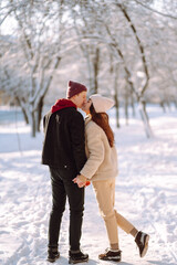 Fototapeta na wymiar Loving couple hugging and kissing in snow forest. Enjoying time together. The concept of youth, love and lifestyle. Winter holidays.
