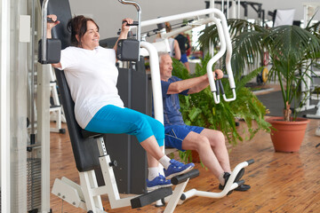 Pensioners training at fitness club. Senior woman exercising on machine at modern gym. People, sport and healthy lifestyle.