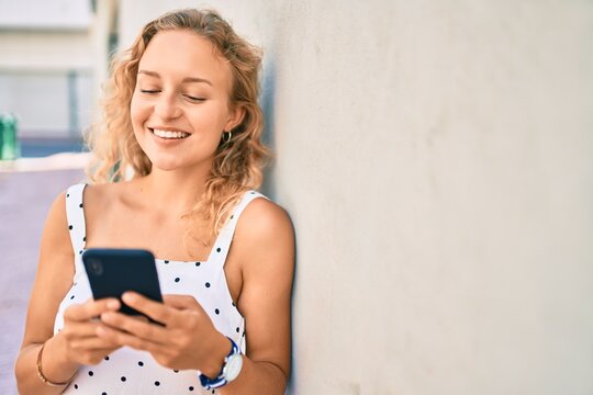 Young beautiful caucasian woman with blond hair smiling happy outdoors using smartphone