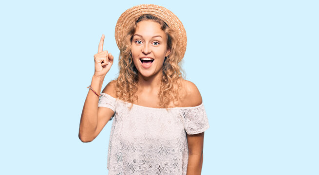 Beautiful caucasian woman wearing summer hat pointing finger up with successful idea. exited and happy. number one.