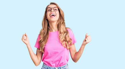 Fototapeta na wymiar Young beautiful caucasian woman with blond hair wearing casual clothes and glasses celebrating surprised and amazed for success with arms raised and open eyes. winner concept.
