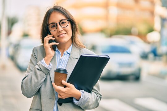 Young hispanic businesswoman talking on the smartphone and drinking take away coffee at the city.