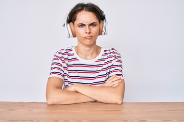 Young hispanic woman using headphones sitting on the table skeptic and nervous, disapproving...
