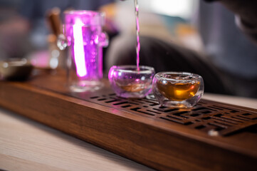 A man passes hot amber tea from a glass flask into a cup. To preserve its strong flavor. Bamboo tray gongfu close-up