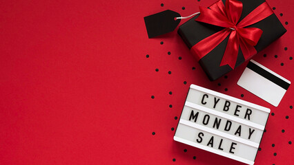 Banner concept for Cyber monday celebration,lettering.White board with text CYBER MONDAY SALE,gift box with red bow,tag,credit card,confetti on red background,top view,flat lay,close-up,copy space