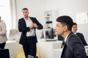 Portrait of a young employee of a developing company in a bright office smiling in the foreground. In the background, business colleagues during a lunch break
