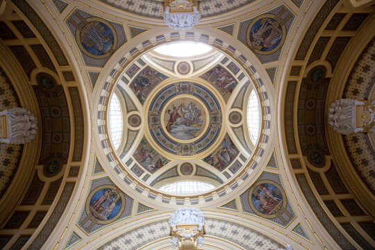 A bottom-up view of the interior of a big building. Brightly lit dome with semicircular windows and religious paintings