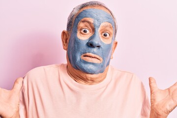 Senior man with grey hair wearing mud mask clueless and confused with open arms, no idea and doubtful face.