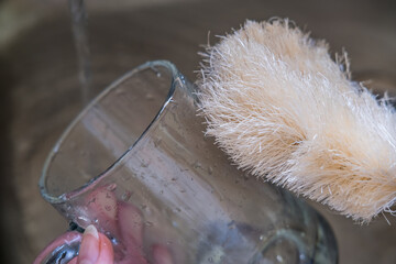 Close up of natural compostable dish washing brush cleaning glass cup by the sink with running tap water. Eco-friendly kitchen and home products. Zero waste sustainable plastic free lifestyle