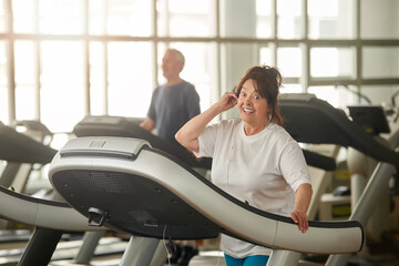 Excited senior woman on treadmill in gym. Happy eldrly woman working out at fitness club. Sport gives energy.