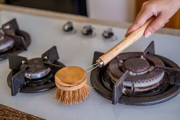 Woman hands cleaning stove cook top with natural compostable washing brush in modern kitchen. Eco-friendly kitchen and home products. Zero waste sustainable plastic free lifestyle