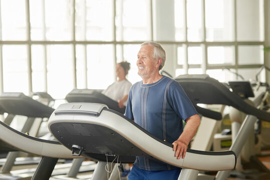 Older Caucasian Man On Treadmill At Gym. Senior Man Training His Body At Gym. Stay Active And Healthy.