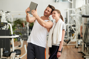 Fototapeta na wymiar Young sporty couple taking selfie with tablet device. Cute athletic couple using digital tablet at gym. People, sport, training and modern technology concept.