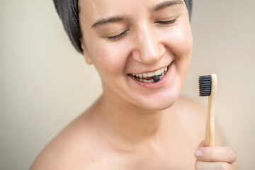 Young woman with towel on head using eco-friendly oral care in bathroom- biodegradable bamboo...