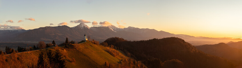 Panorama of golden sunrise at Jamnik, Slovenia with mountains behind the church