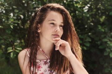 Portrait of a pretty caucasian teen girl with beautiful long curly hair in summer garden