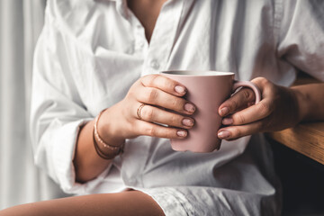Woman in a white t-shirt holds morning coffee in a pink ceramic cup. Manicure. 
