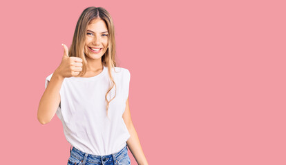 Obraz na płótnie Canvas Beautiful caucasian woman with blonde hair wearing casual white tshirt doing happy thumbs up gesture with hand. approving expression looking at the camera showing success.