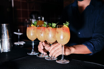Barman gives glasses of orange drink to the client of the nightclub.