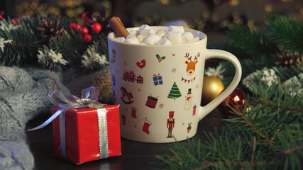 Obraz na płótnie Canvas Hot cocoa with marshmallows, cinnamon, Viennese waffle in white mug, surrounded by winter Christmas tree branches with berries and cones on a wooden table. The concept of a cozy holiday and New Year