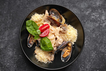 Pasta with seafood, mussels, scallop, rapana and cheese, on a black plate