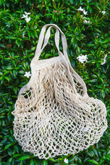 Fototapeta premium Cotton string mesh bag, reusable shopping tote for grocery hanging against green nature background. Zero waste sustainable plastic free lifestyle