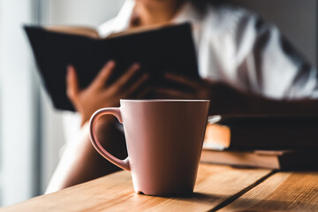 Woman in the morning drinks coffee and reads old book in a white shirt. Education, drink. 