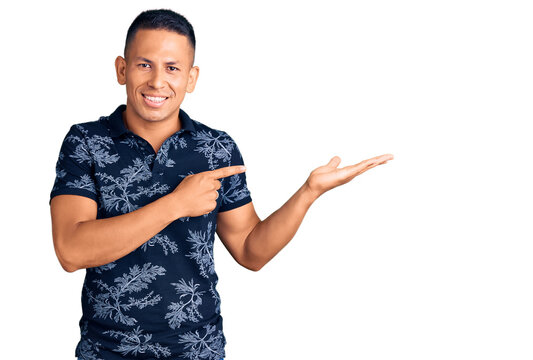 Young handsome latin man wearing casual clothes amazed and smiling to the camera while presenting with hand and pointing with finger.