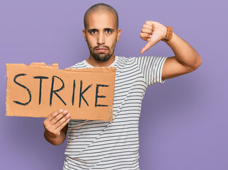Hispanic adult man holding strike banner cardboard with angry face, negative sign showing dislike with thumbs down, rejection concept
