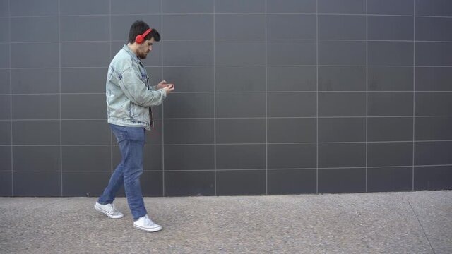 man puts on red headphones and walks while looking at red cell phone