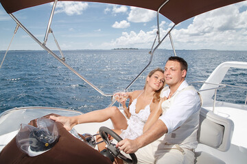 Happy newlyweds in white clothes hug on a white yacht at sea