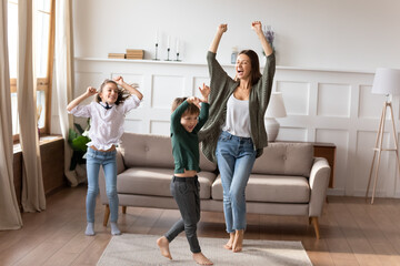Overjoyed young Caucasian mother with two little kids have fun celebrating moving relocation to new home. Happy mom and small children dance on weekend in cozy living room. Entertainment concept.