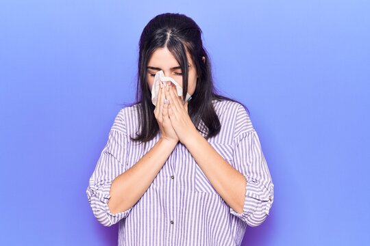 Young hispanic woman illness using paper handkerchief on nose. Standing over isoltated purple background