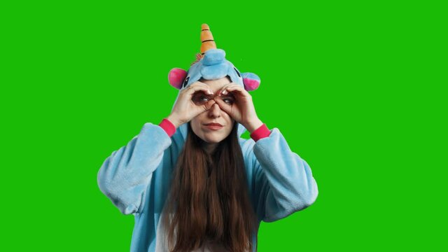 Portrait of a cute young brunette girl in a beautiful unicorn costume on chrome key green background. Smiling and playing. Animator in costume. Unicorn pajamas. 4K video with alpha channel