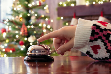 Hand of guest ringing reception bell on desk of guesthouse, hotel at christmas time. Color shining...