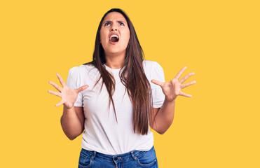 Young beautiful brunette woman wearing casual t-shirt crazy and mad shouting and yelling with aggressive expression and arms raised. frustration concept.