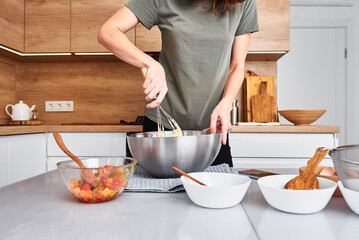 Woman in kitchen cooking a cake. Hands beat the dough with mixer