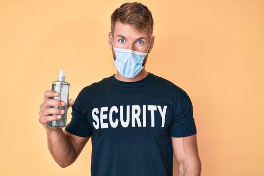 Young caucasian man wearing security t shirt and medical mask holding hand sanitizer gel scared and amazed with open mouth for surprise, disbelief face
