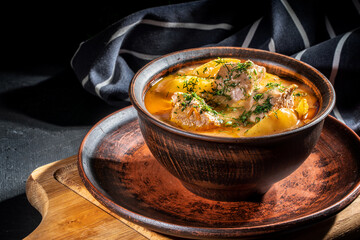 Beef stewed with vegetables( potatoes, carrots, tomatoes, onions) in a clay pot on dark background