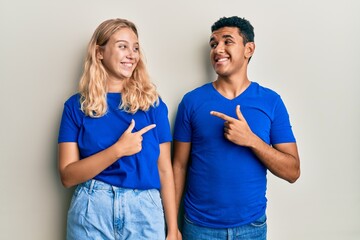 Young interracial couple wearing casual clothes cheerful with a smile on face pointing with hand and finger up to the side with happy and natural expression