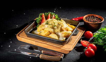 Fried potatoes with cheese and green onion on dark background