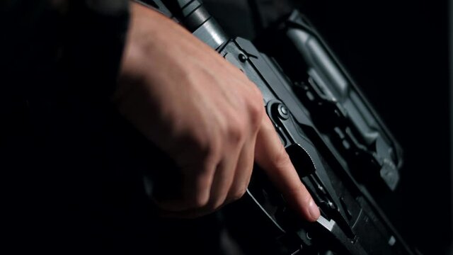 Man in camouflage on a black background removes a rifle from the safety lock