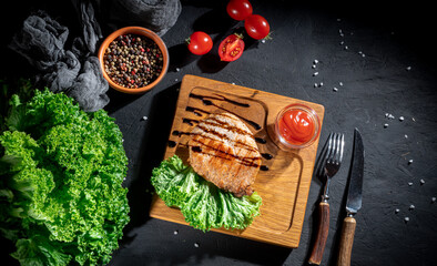 Grilled ribeye beef steak, herbs and spices on dark background. Top view with copy space