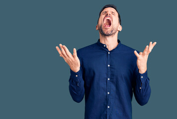 Young handsome man wearing casual shirt celebrating mad and crazy for success with arms raised and...