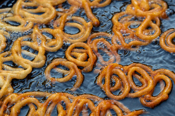 Frying Jalebi batter in oil. Red and orange-colored batter will be dipped into sugar syrup for a sweet taste. Jalebi is a popular sweet snack.