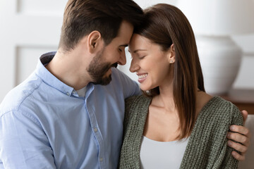 Close up of happy young man and woman lovers touch foreheads enjoy tender intimate moment together. Smiling Caucasian couple feel romantic at home hug embrace show love and care in relationship.