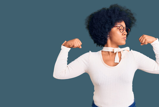 Young african american girl wearing casual clothes and glasses showing arms muscles smiling proud. fitness concept.