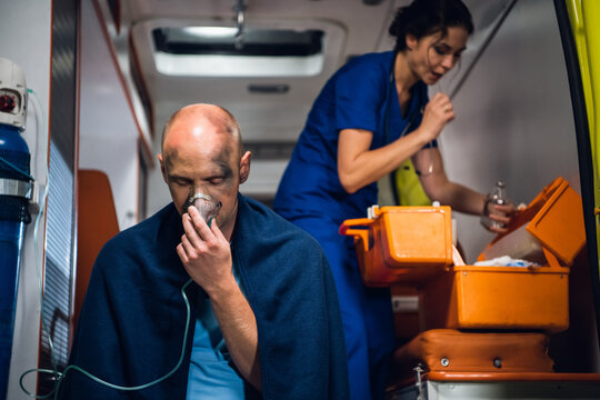 Injured man in a blanket is getting first aid in an ambulance car.